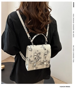 Detailed view of white floral butterfly print backpack worn by model against a white wall