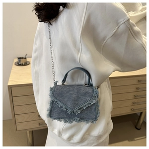 Detail of light blue denim crossbody bag with frayed edges and silver chain strap
