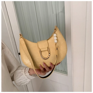 Detail of cream faux crocodile underarm bag featuring a gold D-buckle and pearl strap