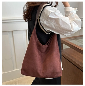 Détail d'un grand sac hobo en daim marron foncé porté à l'épaule pour un usage quotidien