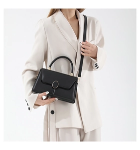 Model showcasing a structured black leather handbag with a gold oval buckle and top handle