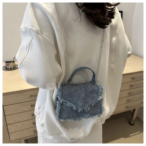 Detail of blue denim crossbody bag featuring frayed fringe edges and silver chain strap