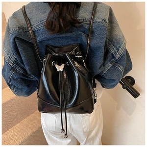 Detail of black drawstring bucket bag featuring a metal butterfly buckle and glossy finish