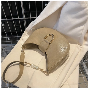 Macro detail of beige crocodile embossed leather saddle bag with gold buckle and pearl strap