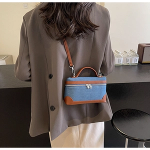 Detail view of denim patchwork crossbody bag with brown leather trim worn by a model