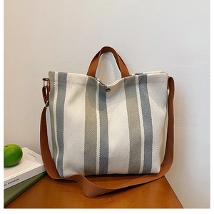 Détail du sac cabas en toile rayée avec anses marron et fermeture par bouton-pression en métal