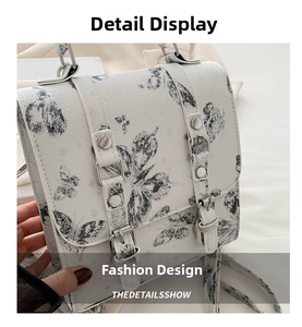 Close-up of white shoulder bag featuring black butterfly prints and silver buckles