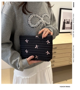 Detail einer schwarzen gesteppten Cord-Clutch mit rosa gestickten Schleifen am Modell