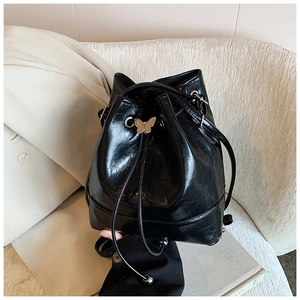 Detailed macro view of black glossy bucket bag with metallic butterfly buckle and drawstring