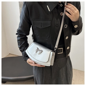 Detail of silver metallic crossbody bag with bow buckle worn over a black leather jacket
