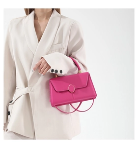 Detail of rose pink leather handbag featuring a round gold metal buckle and top handle