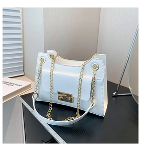 Detail of white PU leather square bag with gold chain strap on a black wooden surface