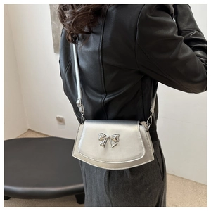 Detail of silver metallic crossbody bag with bow buckle and adjustable strap