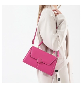 Side view of a magenta crossbody square bag with gold oval buckle on a light blazer