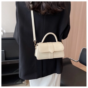 Cream white leather crossbody bag shown on a model in a sleek modern indoor setting