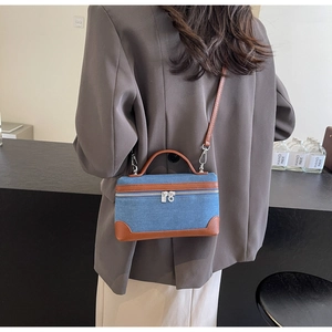 Detail of blue denim and brown leather mini box bag worn as a crossbody accessory