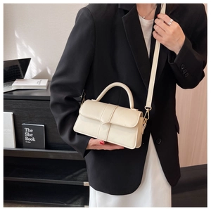 Detail of a beige crossbody bag with top handle and gold hardware on a fashion model