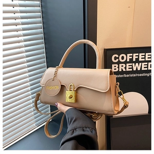 Detail of beige shoulder bag with gold clasp and circular fashion charm in hand