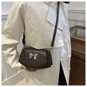 Deep brown crossbody bag with silver bow buckle worn on cream coat for 2024 fashion