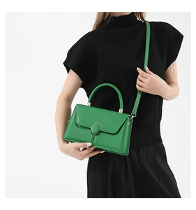 Detail of green leather handbag featuring oval metal buckle and textured stitching