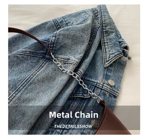 Detail view of brown leather shoulder strap with silver metal chain on denim jacket
