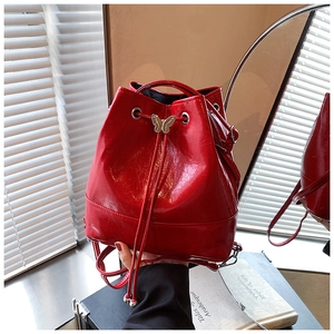 Detail of red glossy drawstring bucket bag with gold butterfly clasp and crinkled texture