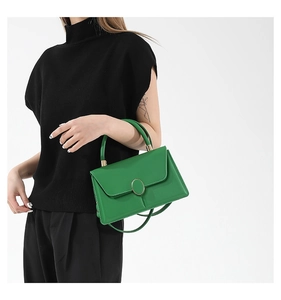 Detail of a bright green leather crossbody bag with a golden oval metallic lock buckle