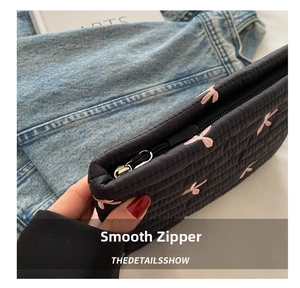 Detail of smooth metal zipper and pink embroidered bow on black quilted corduroy bag