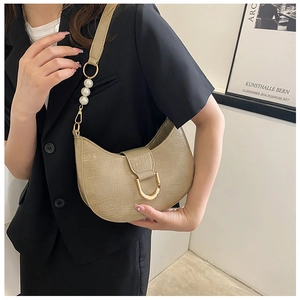 Detail of beige crescent bag featuring crocodile texture and elegant pearl shoulder strap