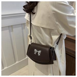 Brown crossbody bag with silver bow detail worn over a stylish beige trench coat