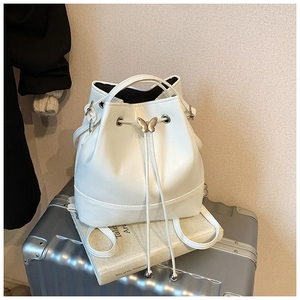 Detail of white bucket bag with drawstring closure and butterfly metal lock on luggage