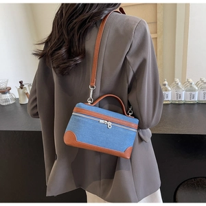 Detail of denim crossbody bag with brown leather trim shown on a model in a lifestyle setting