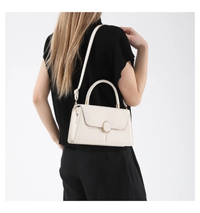 Model wearing a stylish ivory crossbody bag with a gold ring buckle and top handle