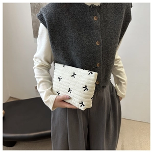 Detailed view of white quilted cosmetic bag with black ribbon bow embroidery in a model hand