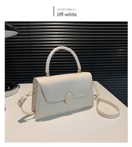 Minimalist beige textured crossbody bag with gold buckle and top handle shown on white desk