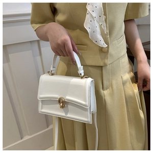 Dettaglio di una borsa bianca strutturata con chiusura dorata circolare e pelle sintetica