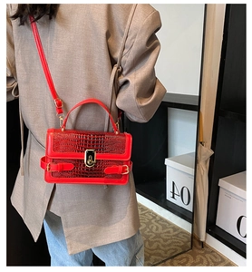 Detail of red crocodile texture handbag with gold hardware worn over a beige blazer