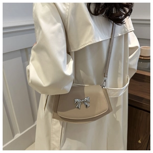 Detail of cream crossbody bag featuring a silver metal bow accent and flap closure