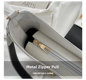 Close-up of golden metal zipper pull on white crocodile embossed leather handbag