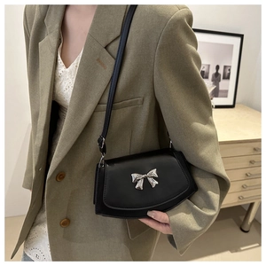 Close-up of black crossbody bag with silver bow detail on a stylish khaki blazer