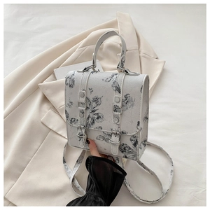 Detail of grey butterfly print bag featuring buckle straps on a beige blazer background
