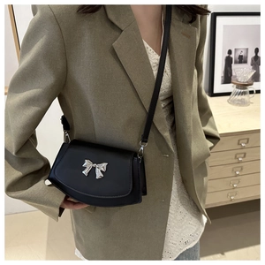 Detail of black crossbody fan bag featuring a silver metal bow and slim leather strap