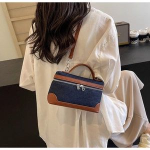 Detail of blue denim crossbody bag with brown leather trim worn by a model in casual setting
