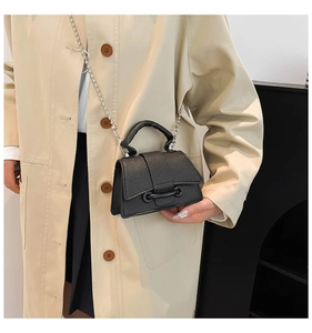 Détail du mini sac noir grainé avec chaîne à boules argentées sur un trench beige