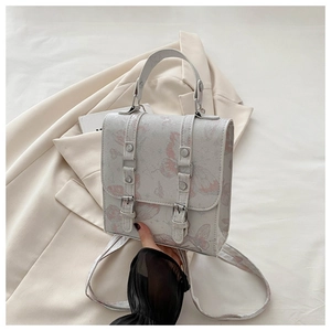 Detail of grey crossbody bag featuring pink butterfly print and decorative buckles