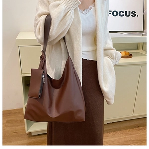 Detail of a large dark brown tote bag with a matching small zipper pouch on a model