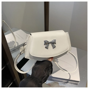 Detail of white mini crossbody bag featuring a 3D silver metal bow buckle and PU strap