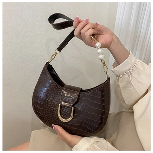 Detail of brown croc-effect saddle bag with pearl handle and golden D-buckle closure