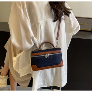 Detail of vintage denim and brown leather stitching on a small crossbody bag with dual zippers
