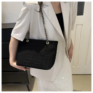 Détail d'un sac cabas en tweed noir avec chaîne dorée sur un blazer blanc